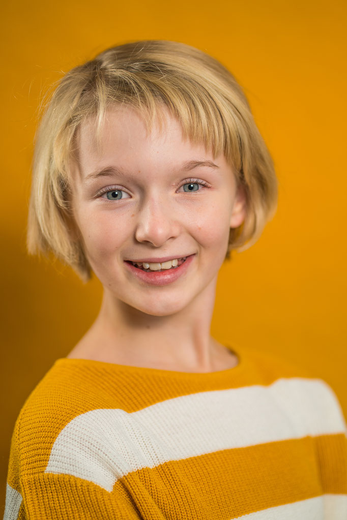 Lächelndes Mädchen auf einem Schulfoto mir orangenem Hintergrund