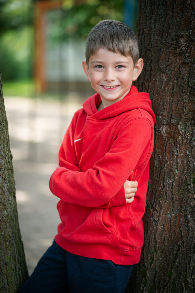 Lächelnder Junge an einem Baum angelehnt auf einem modernen Schulfoto