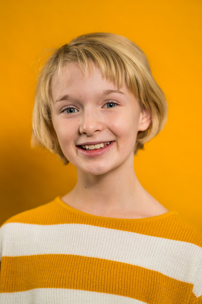 Fröhliches Mädchen vor orangenem Hintergrund auf einem Schulfoto